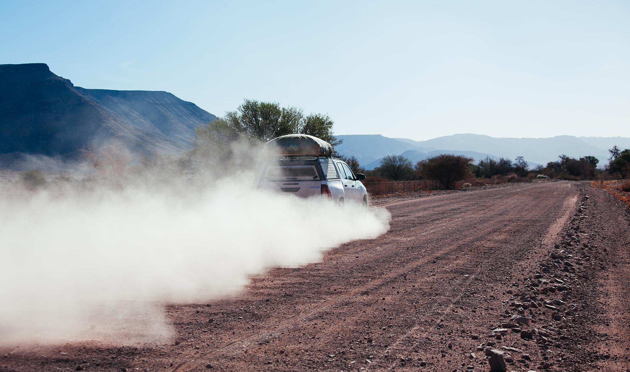 Dust cloud behind a rental car on dirt road