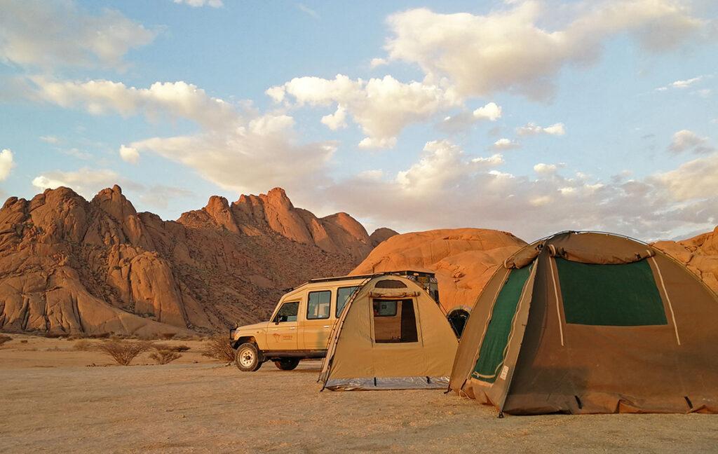 Aufbau für Campingurlaub in Namibia: Campingplatz, Zelte und Safarifahrzeug, im Hintergrund Bergkette