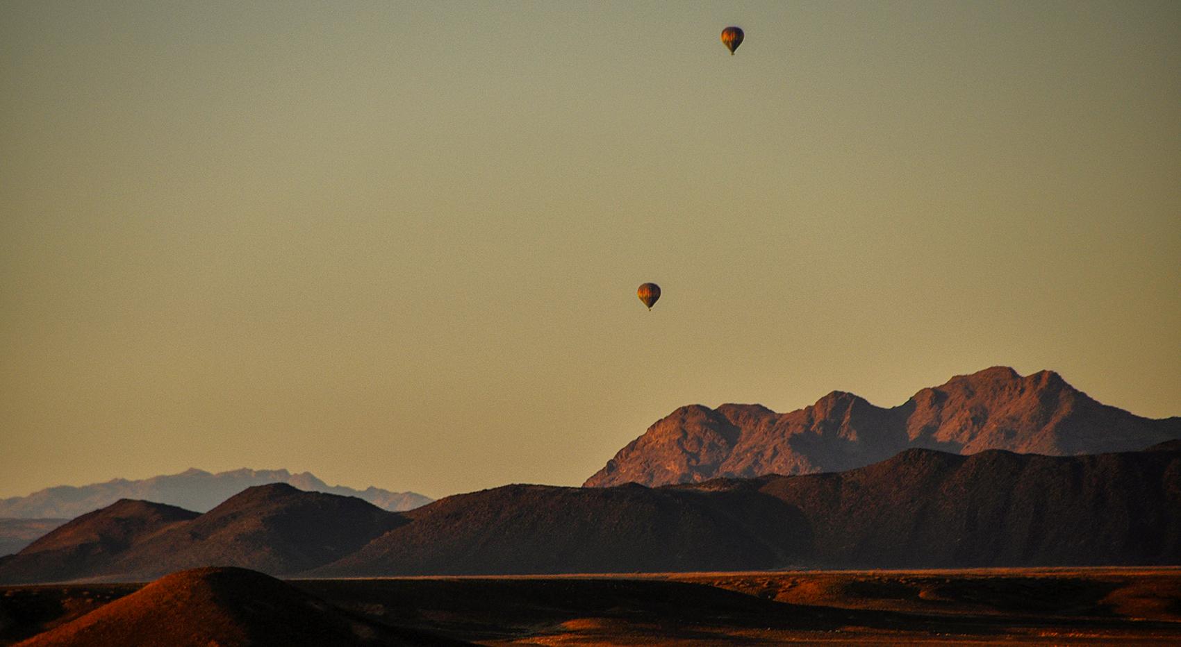 Two hot-air balloons on safari through the mountainous landscape of the Namib Desert.