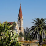 Christ Church in Windhoek, Namibia, viewed from a distance with palms in the foreground and a clear azure sky behind.