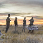 Three guests standing in the vast wilderness enjoying a sundowner with their guide who is taking them on an evening game drive.