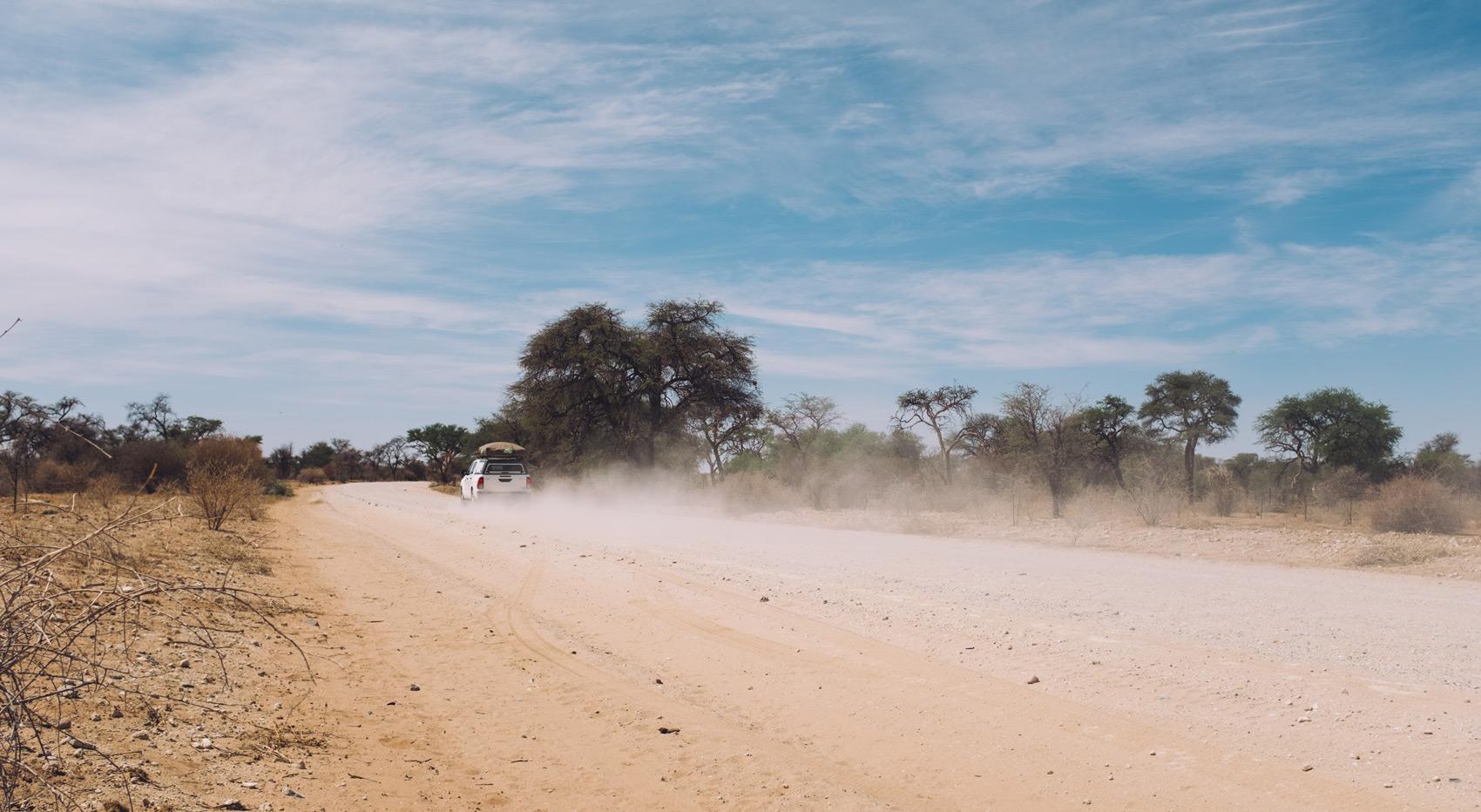 A car creating a dust cloud on a dirt road in Namibia.