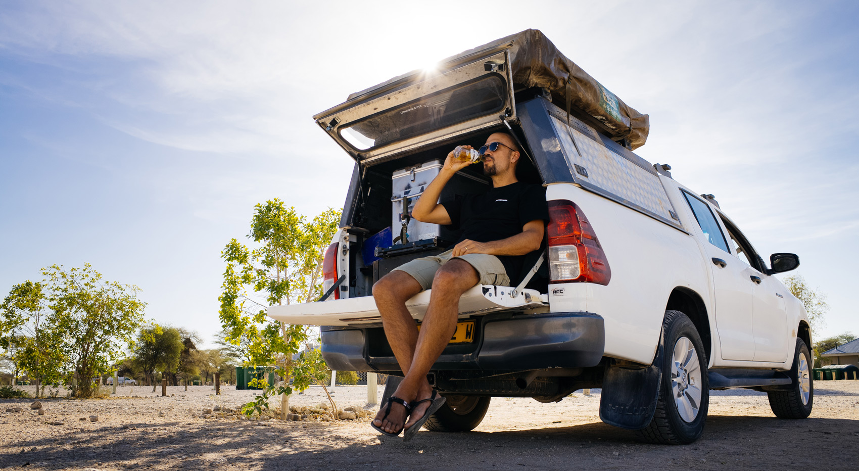 A self-drive tourist sitting in the boot of his car, enjoying a drink.