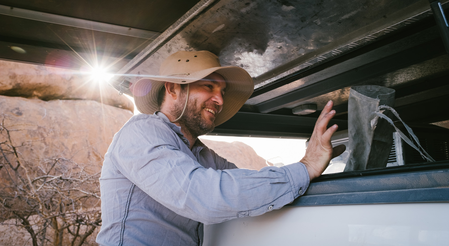 A tourist getting something out of his car with roof tent.