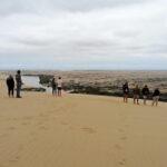 Eine Gruppe Reisender schaut von einer Sanddüne aus über den Kunene Fluss