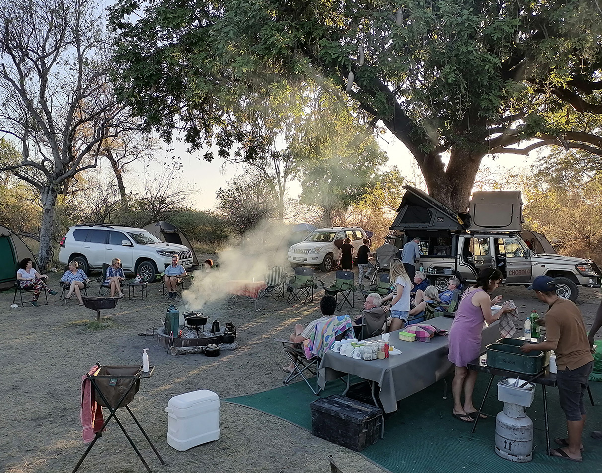 Eine Gruppe von Reisenden an einem Campingplatz mit aufgebauten Zelten, Küche und Stühlen.