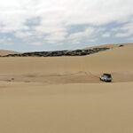 Ein 4x4-Fahrzeug auf einer Skeleton Coast Selbstfahrerreise fährt eine Sanddüne hinauf.