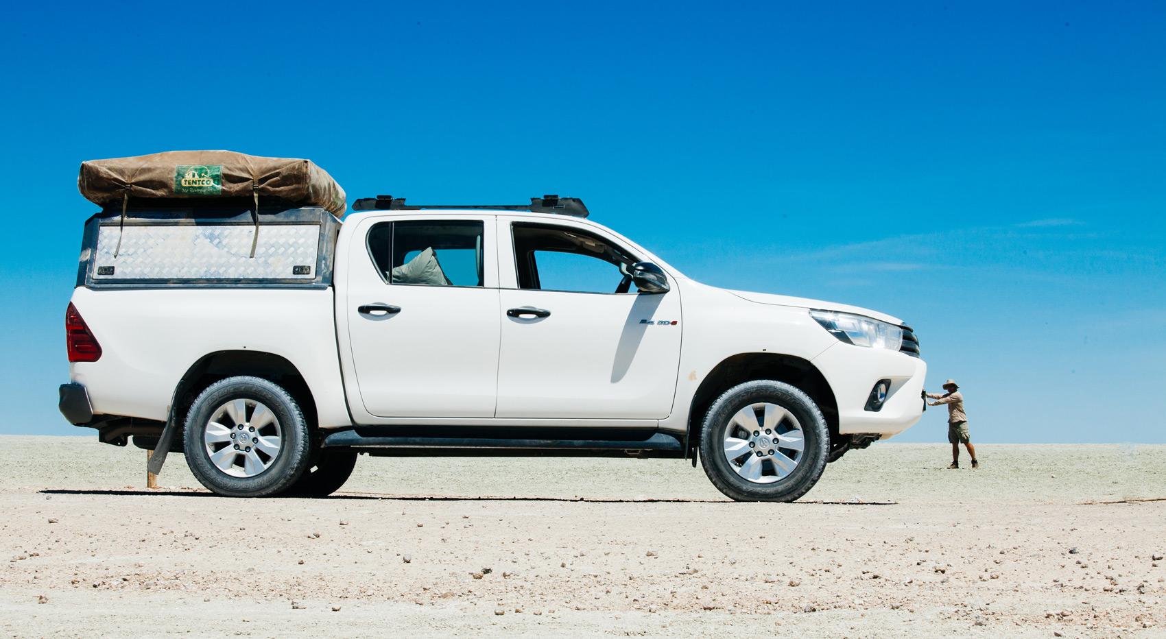 A self-drive vehicle in Etosha National Park with a guest standing far behind it, creating a playful optical illusion that makes the car look enormous.