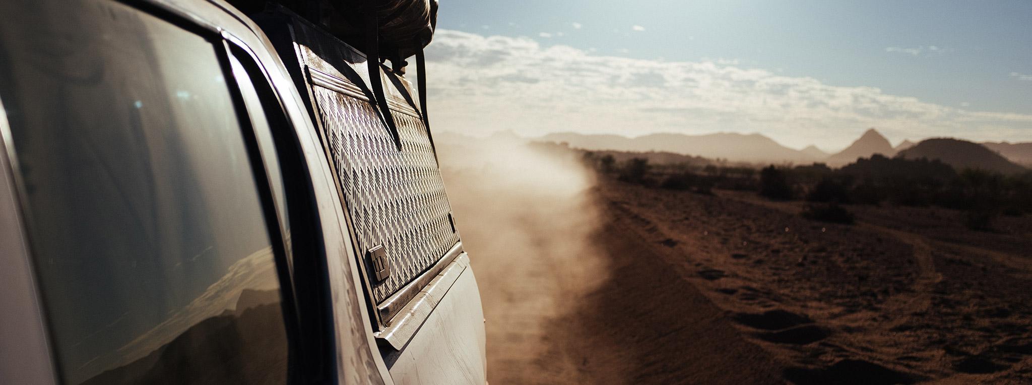 Closeup of a guided self-drive vehicle with roof top tent on a dusty road in Namibia.