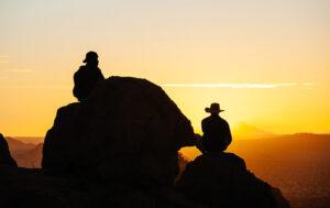 Silhouette of guide and guest sitting on a large boulder at sunset.