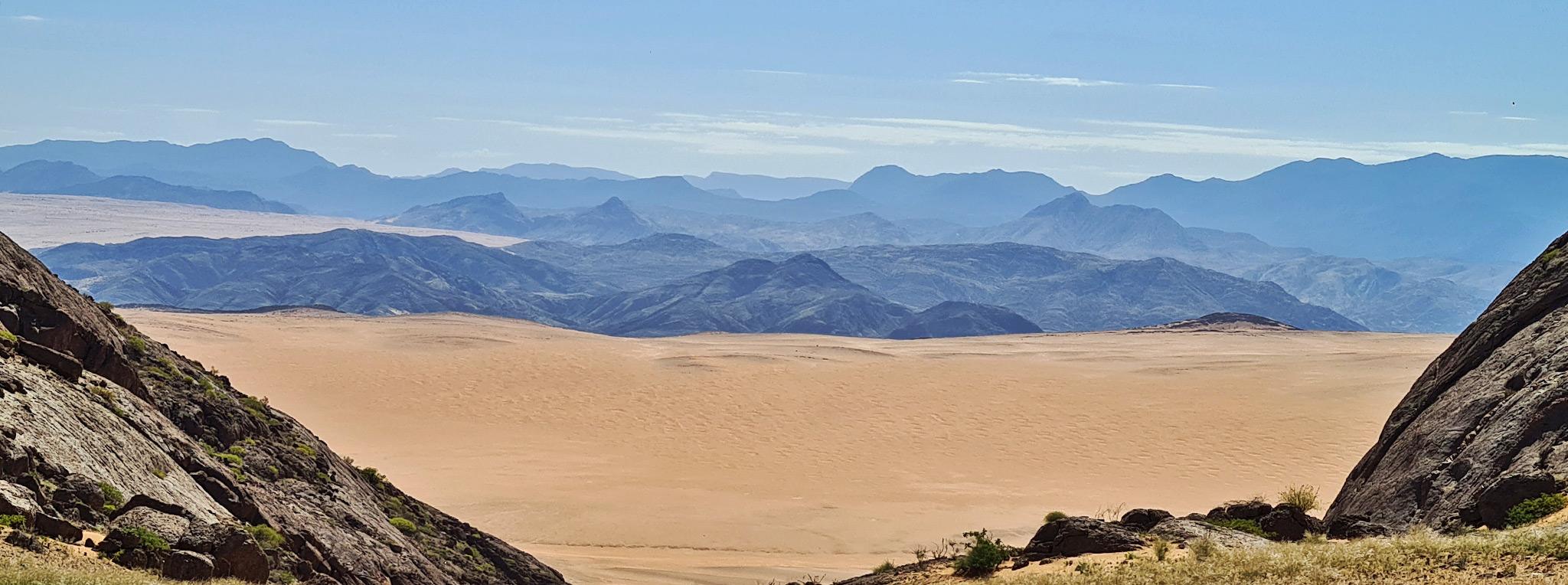Blick auf das Hartmann's Valley im Norden Namibias mit einer Bergkette am Horizont und blauem Himmel darüber.