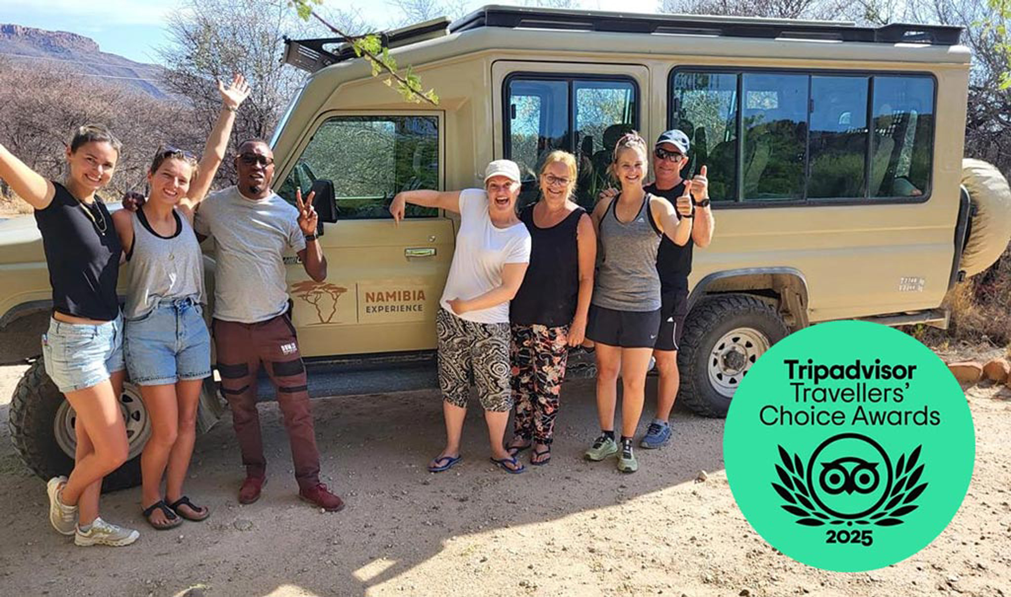 A photo of Namibia Experience guide and guests infront of a safari vehicle and travellers choice award badge.