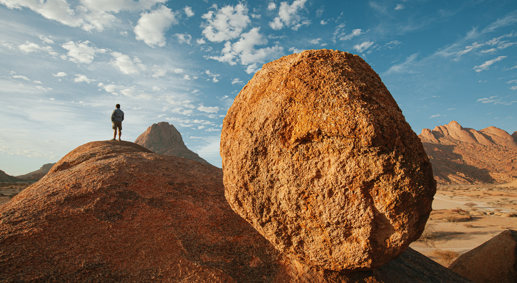 A big boulder with hiker and Spitzkoppe in the background.