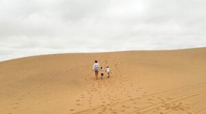 A mother walking up a sand dune with her two children in Namibia.